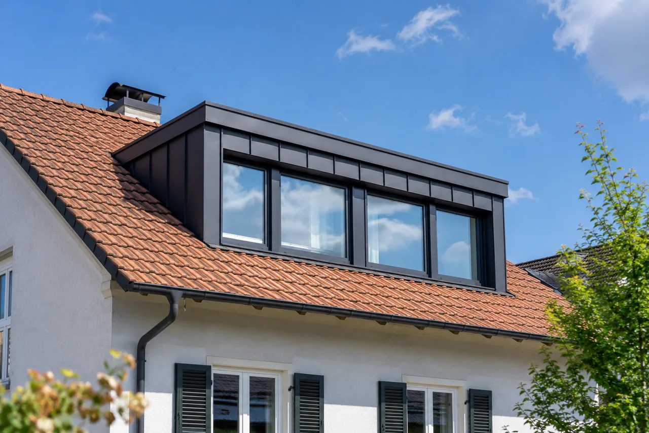 Nahaufnahme einer modernen Dachgaube mit großen Fenstern auf einem roten Ziegeldach, die beim Dachausbau für den Nachwuchs für mehr Licht und Wohnfläche sorgt.